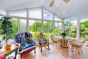 Et solarium med et glasbord, fletstole og en gyngestol med et mønstret tæppe.