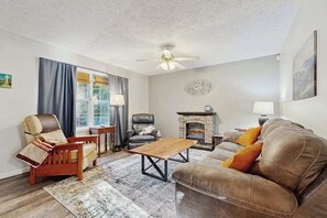 Ein Wohnzimmer mit Kamin, Ledersofas, einem Holztisch und Deckenventilator.