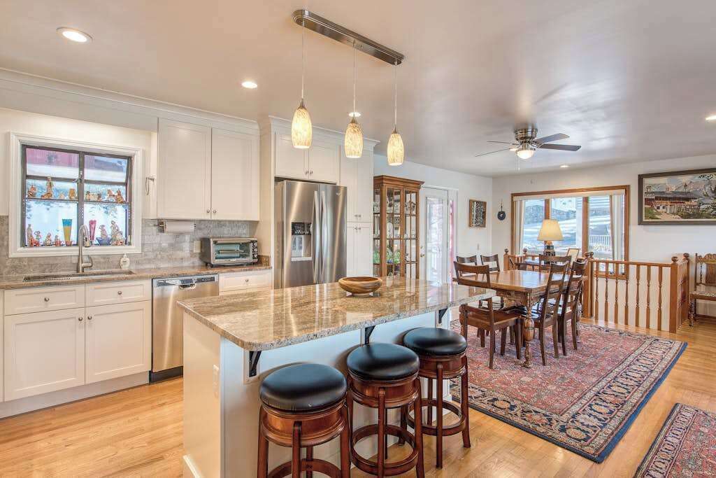 A kitchen with a large island, bar stools, a dining table with chairs, and a ceiling fan.