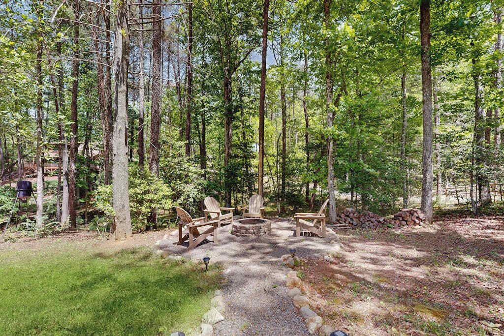 Un terrain de camping boisé, équipé d’un foyer, de chaises en bois et d’un sentier de gravier.