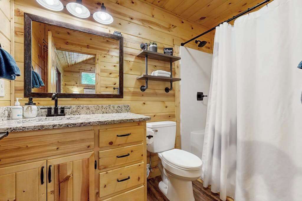 Un bagno in una cabina di legno con lavabo su un piano in granito, uno specchio grande, un water e una tenda per la doccia.