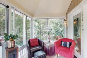 Ein Wintergarten mit großen Fenstern, einem Kamin, einem Tisch mit einer Vase und zwei Stühlen.