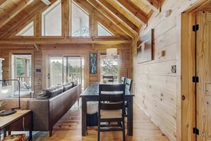 Ein Interieur einer Holzhütte mit Esstisch, Stühlen, einer Couch und einem großen Fenster.