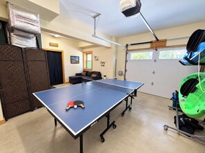Ein Tischtennisch in einem Raum, der einen Deckenventilator, ein Fahrrad und eine Garagentür beherbergt.