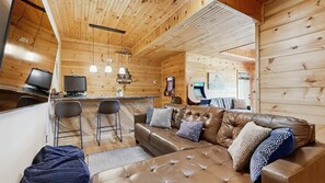 Ein gemütliches Blockhausschlafzimmer mit einem Ledersofa, Barhocker und einem Fernseher.