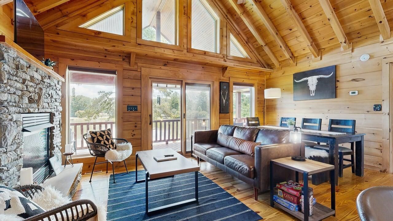Interior acogedor de una cabaña con chimenea de piedra, un sofá, una mesa de centro y una mesa de comedor.