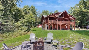 Un chalet doté d’une terrasse, entouré d’arbres, avec un foyer et des chaises.