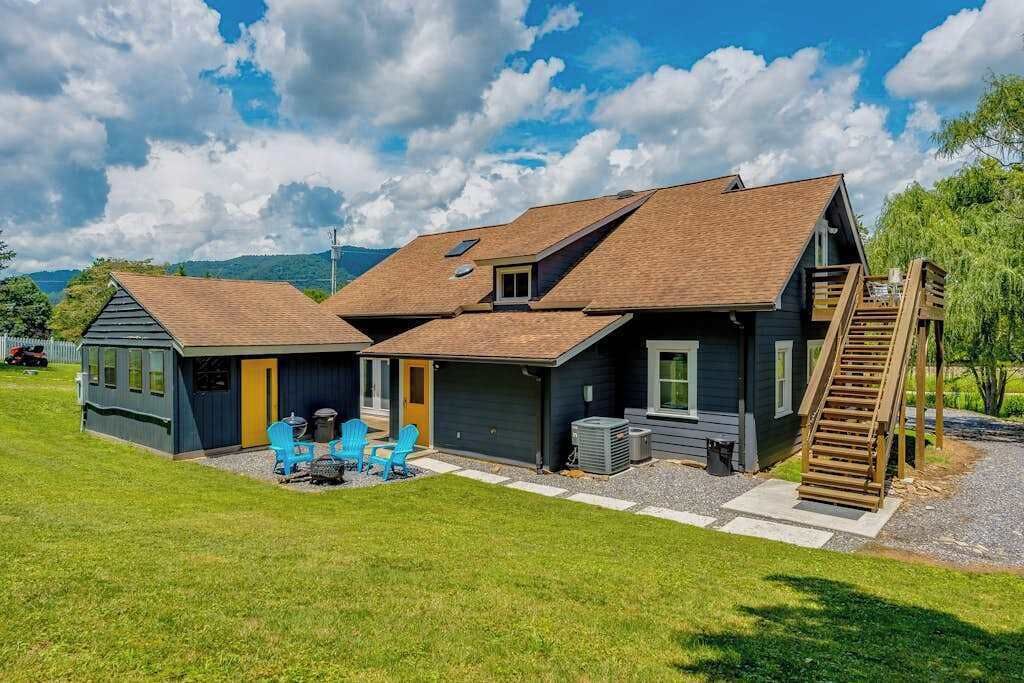 Une maison à deux étages dotée d’un patio couvert, d’un escalier en bois et d’un petit espace extérieur aménagé pour s’asseoir.