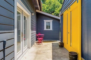 Un espacio exterior estrecho con una mesa y sillas, una puerta y una ventana.