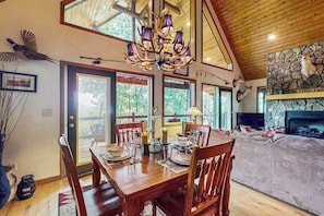 A dining area with a wooden table and chairs, a chandelier, and a stone fireplace with mounted deer heads. - Wildcat Retreat (Murphy)