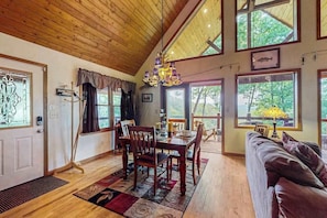 A dining area with a wooden table and chairs, a chandelier, and large windows with a view of greenery. - Wildcat Retreat (Murphy)