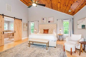 Ein Schlafzimmer mit einem großen Bett, einer Bank, einem Sessel, einem Nachttisch und einem Deckenventilator.