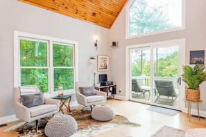 Ein geräumiges Wohnzimmer mit großen Fenstern, Holzboden und einem Balkon mit Gartenmöbeln.