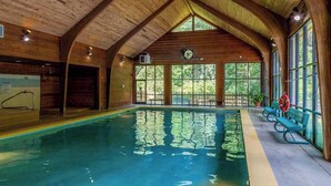 Una piscina interior con vigas de madera, ventanas grandes y una silla para salvavidas.