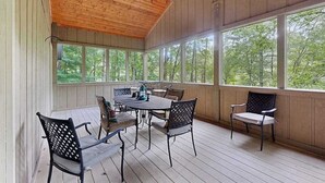 Un espacio al aire libre techado con mesa y sillas, ventanas amplias y un ventilador de techo.