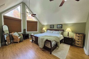 A bedroom with a bed, a chair, a nightstand, a lamp, a mirror, and a window. - Mountain-View Escape on Rumbling Bald’s 14th & 15th Holes (Lake Lure)