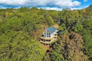 A house surrounded by dense forest, with a large deck and multiple windows. - Mountain-View Escape on Rumbling Bald’s 14th & 15th Holes (Lake Lure)