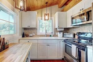 A kitchen with white cabinets, a wooden countertop, a stove, a microwave, and a window.