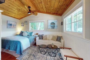 A bedroom with a bed, a white sofa, two round tables, and a ceiling fan.