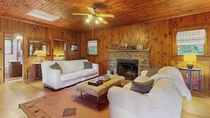 Une pièce aux murs lambrés, avec une cheminée, un canapé, une table basse et un ventilateur de plafond.