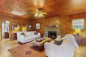 Una habitación con paneles de madera, una chimenea, un sofá, una mesa de centro y un ventilador de techo.