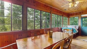 L’intérieur d’un chalet en bois comprend une table à manger, des chaises, un lit et de grandes fenêtres.
