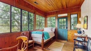 Une pièce de style cabane en bois, comprenant un lit, une chaise, une table et de grandes fenêtres.