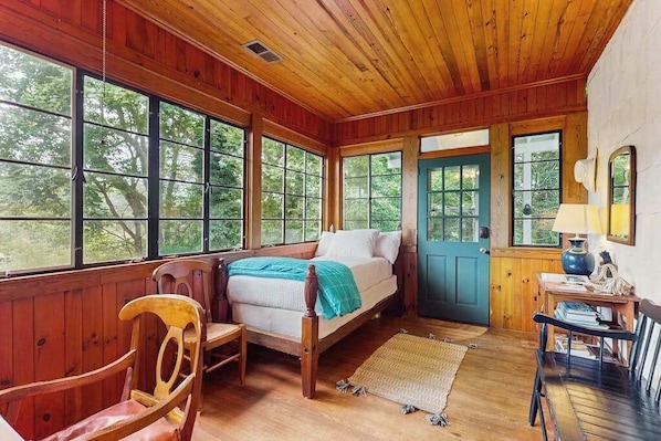 Una habitación de cabaña de madera con una cama, una silla, una mesa y ventanas amplias.