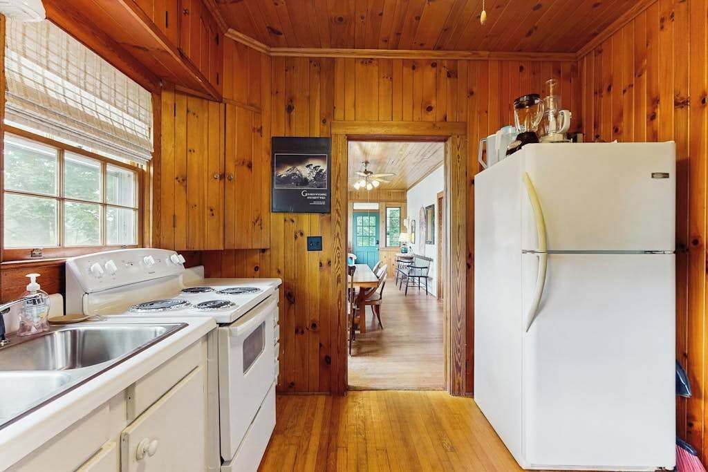 A wooden-paneled kitchen with a stove, sink, and refrigerator.