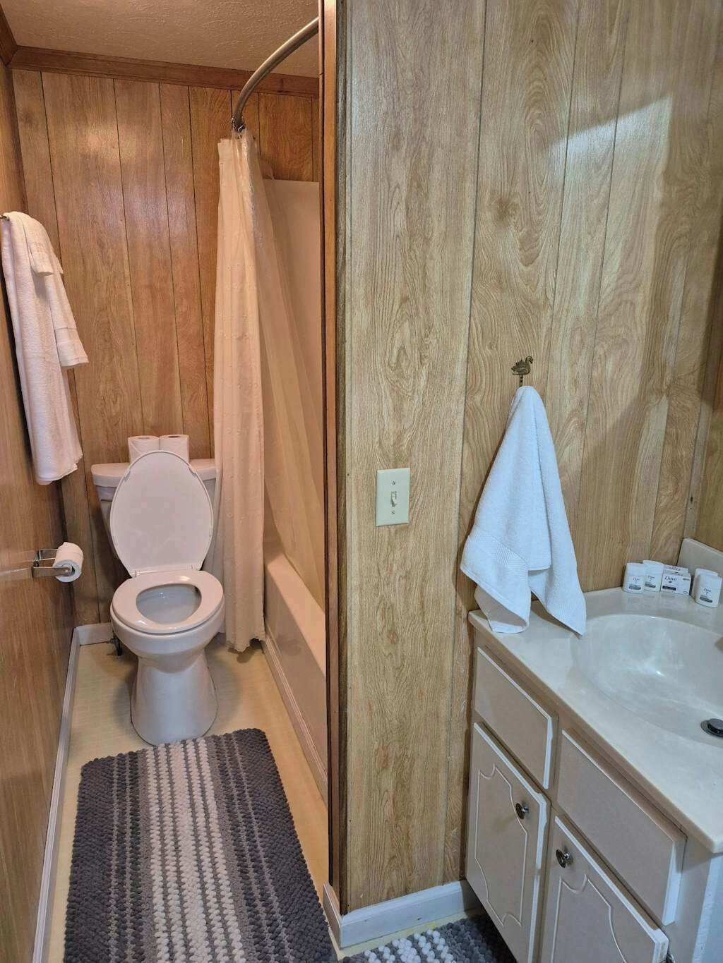 A bathroom with a wooden wall, a white toilet, a shower curtain, a sink with a mirror, and a towel rack.