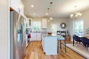 A modern kitchen with a central island, stainless steel appliances, and a dining area with black chairs. - Secluded Mill Spring Retreat: Stunning Views, Luxury Amenities (Mill Spring)