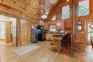 Ein Holzblockhaus-Interieur mit Küche, Essbereich und Deckenventilator.