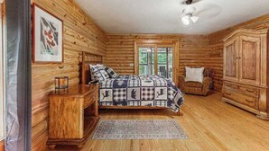 Un dormitorio tipo cabaña de madera con una cama, una silla, un armario y un ventilador de techo.