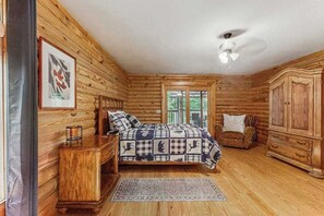 Ein Schlafzimmer in einer Blockhütte mit einem Bett, einem Sessel, einem Kleiderschrank und einem Deckenventilator.