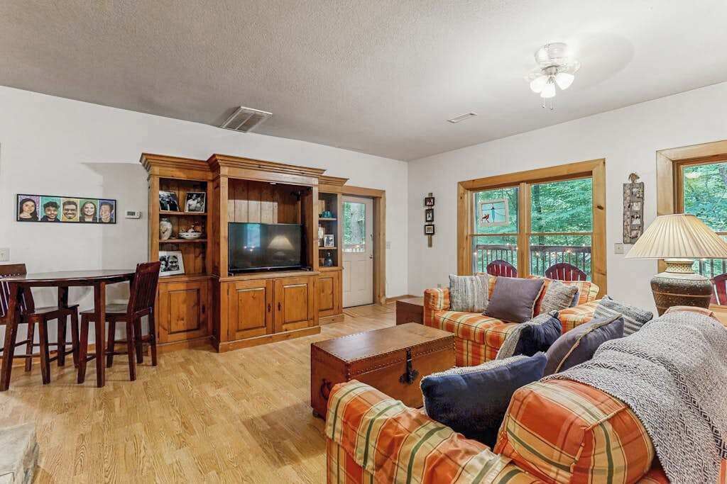 Un salon comprenant un meuble de rangement en bois pour les appareils multimédias, un téléviseur, un ensemble de canapés et une table à manger avec des chaises.
