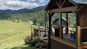 Uma cabana de madeira com varanda e vista para uma paisagem verde e montanhas.