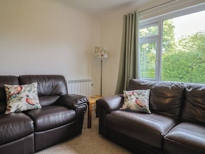 A living room with two leather sofas, each with a floral pillow, a floor lamp, and a window with curtains. - 2 North Road (Dorchester)