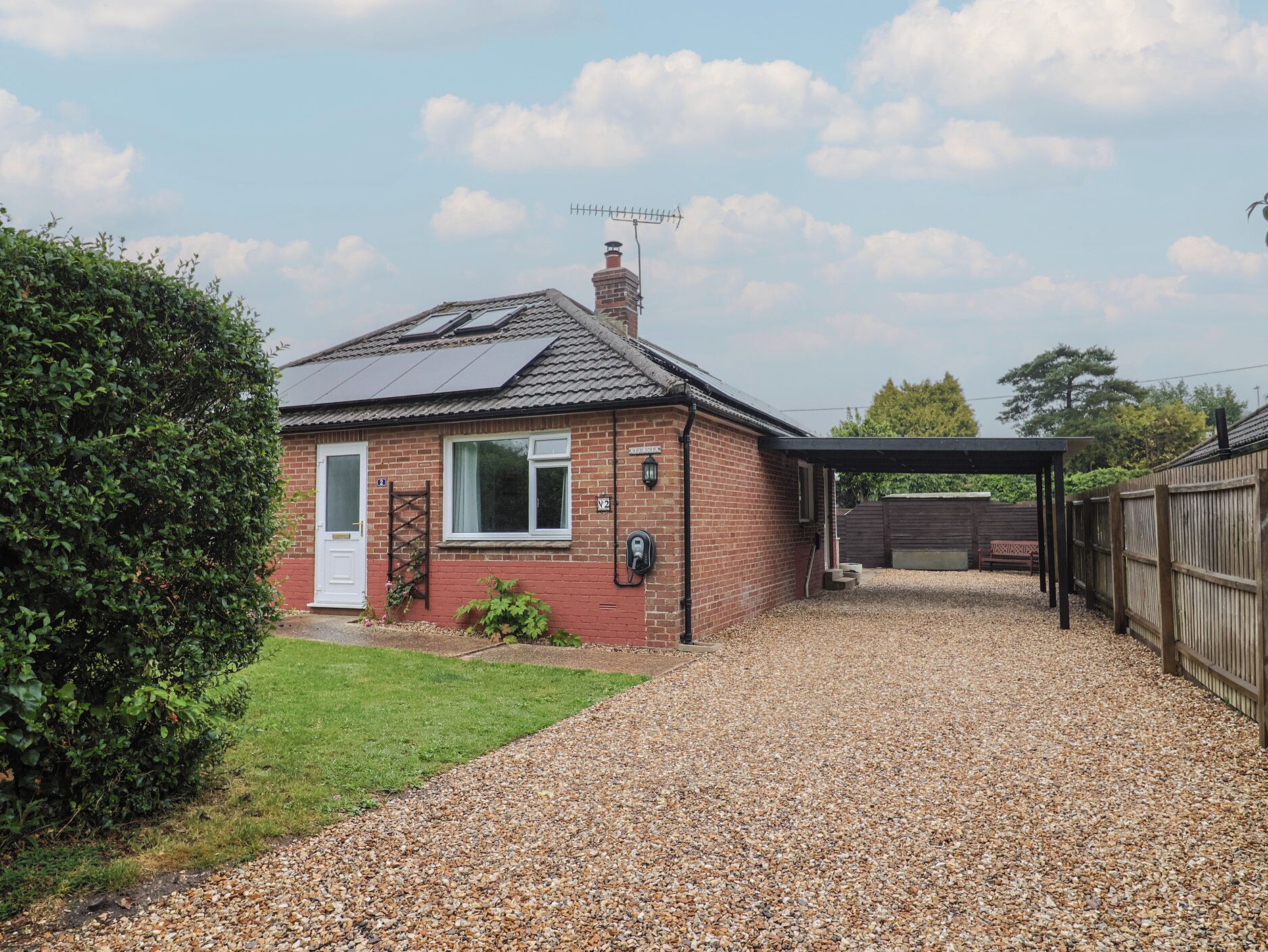 A house with a gravel driveway, a covered carport, and a brick chimney.