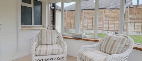 A sunroom with two wicker chairs, large windows, and a view of a wooden fence.
