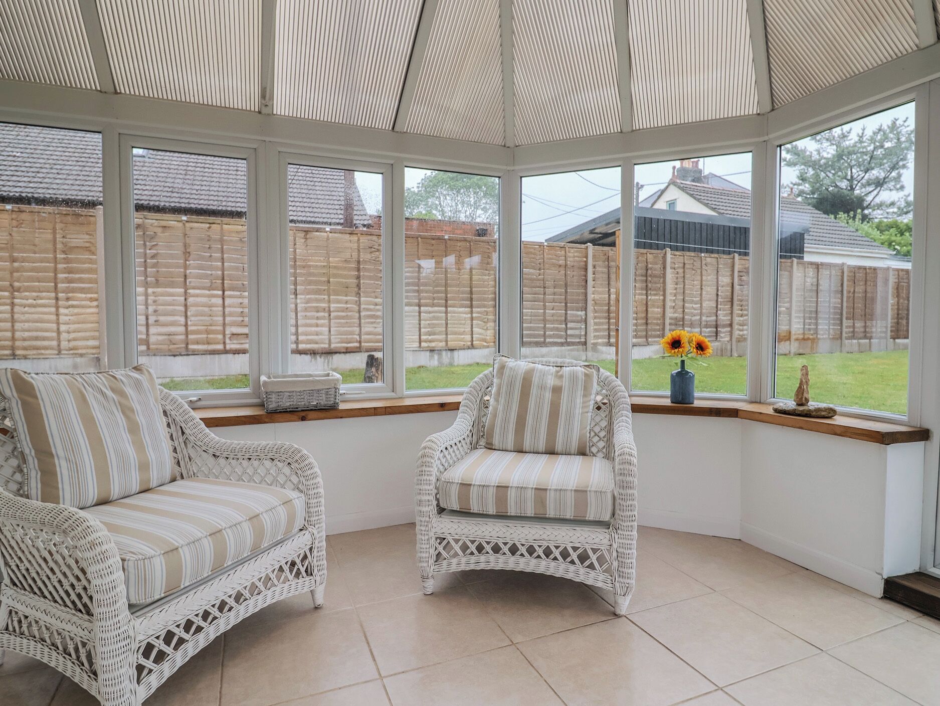 A conservatory with wicker furniture, large windows, and a view of a garden.