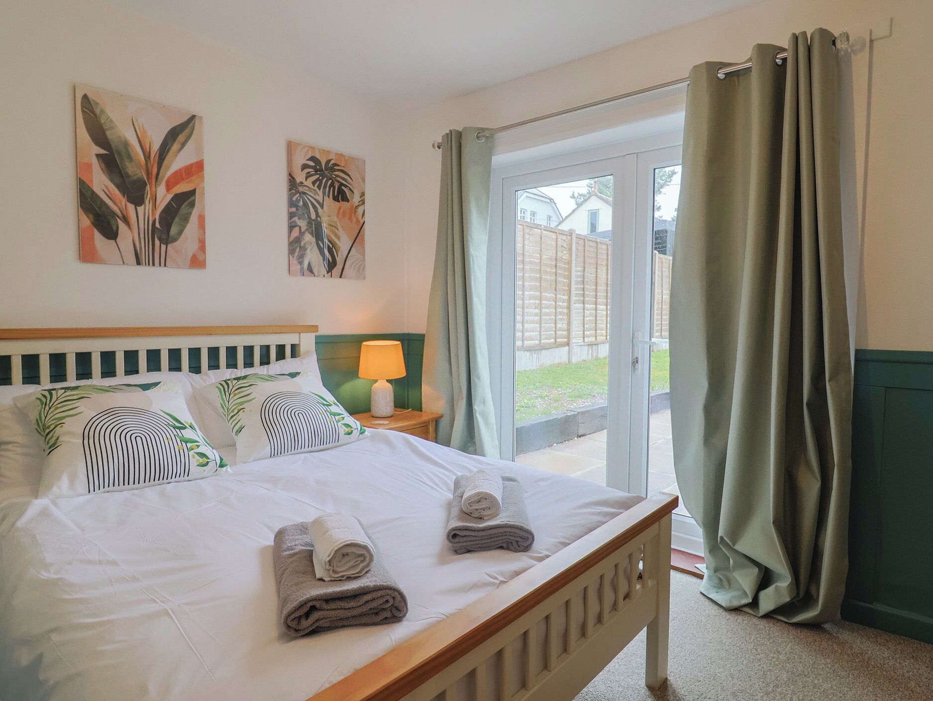 A bedroom with a bed, pillows, a nightstand with a lamp, and a view through a glass door.