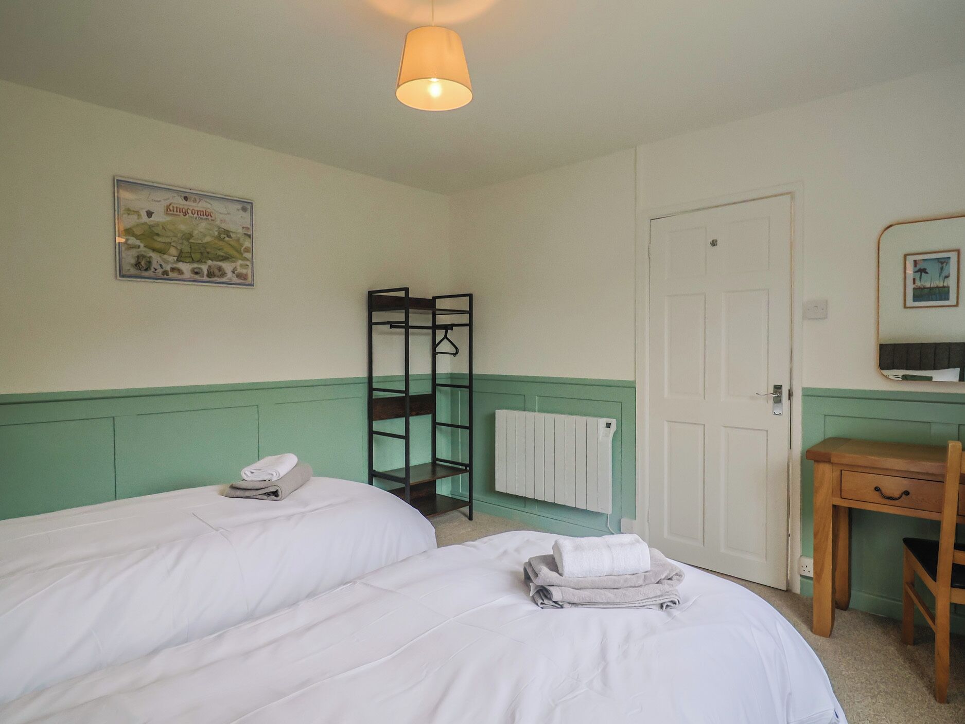 A hotel room with two beds, a radiator, a wooden chair, a small table, and a hanging light fixture.