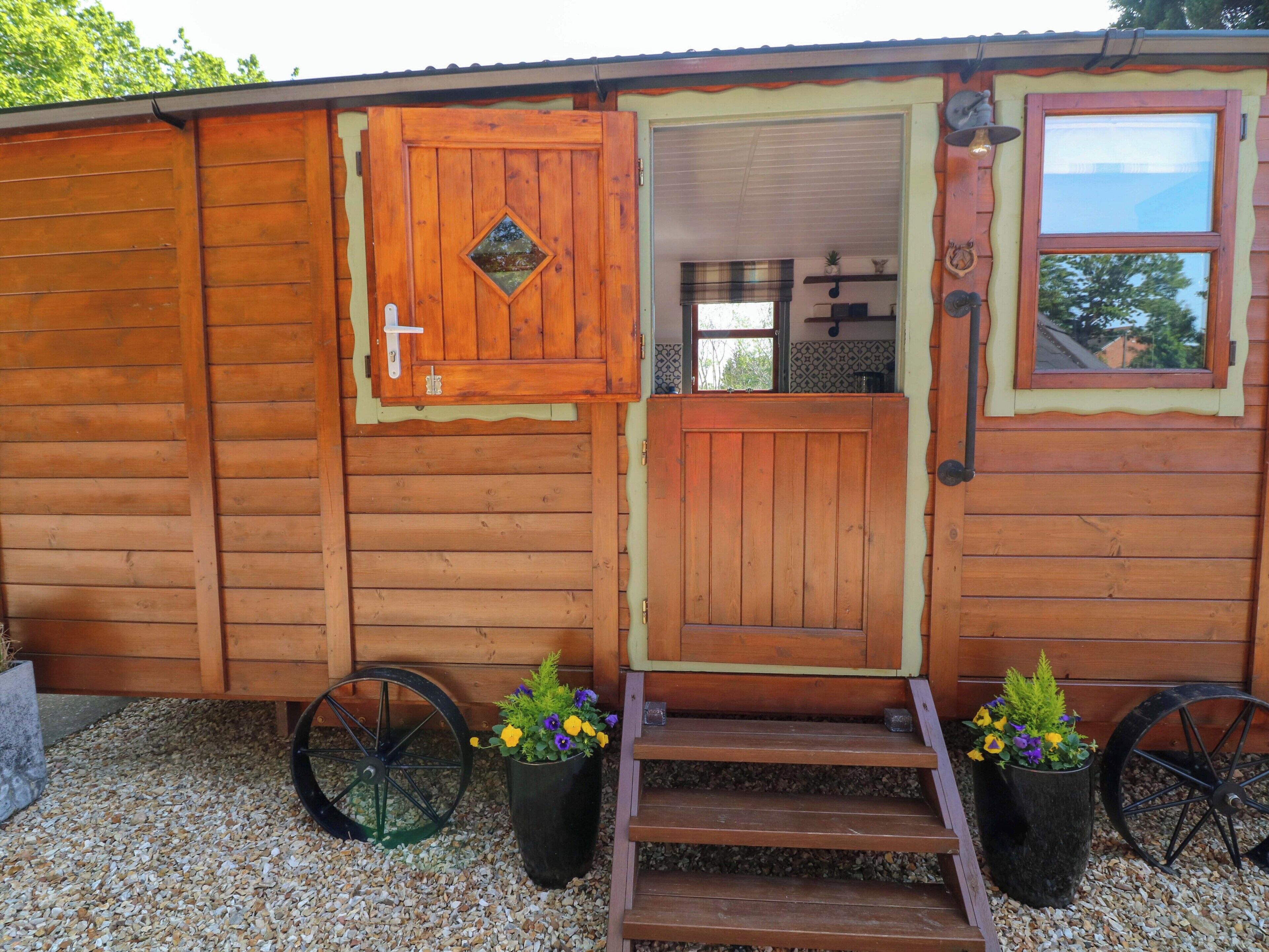 A wooden cabin with a front door, two potted plants, a window, and a small porch area.