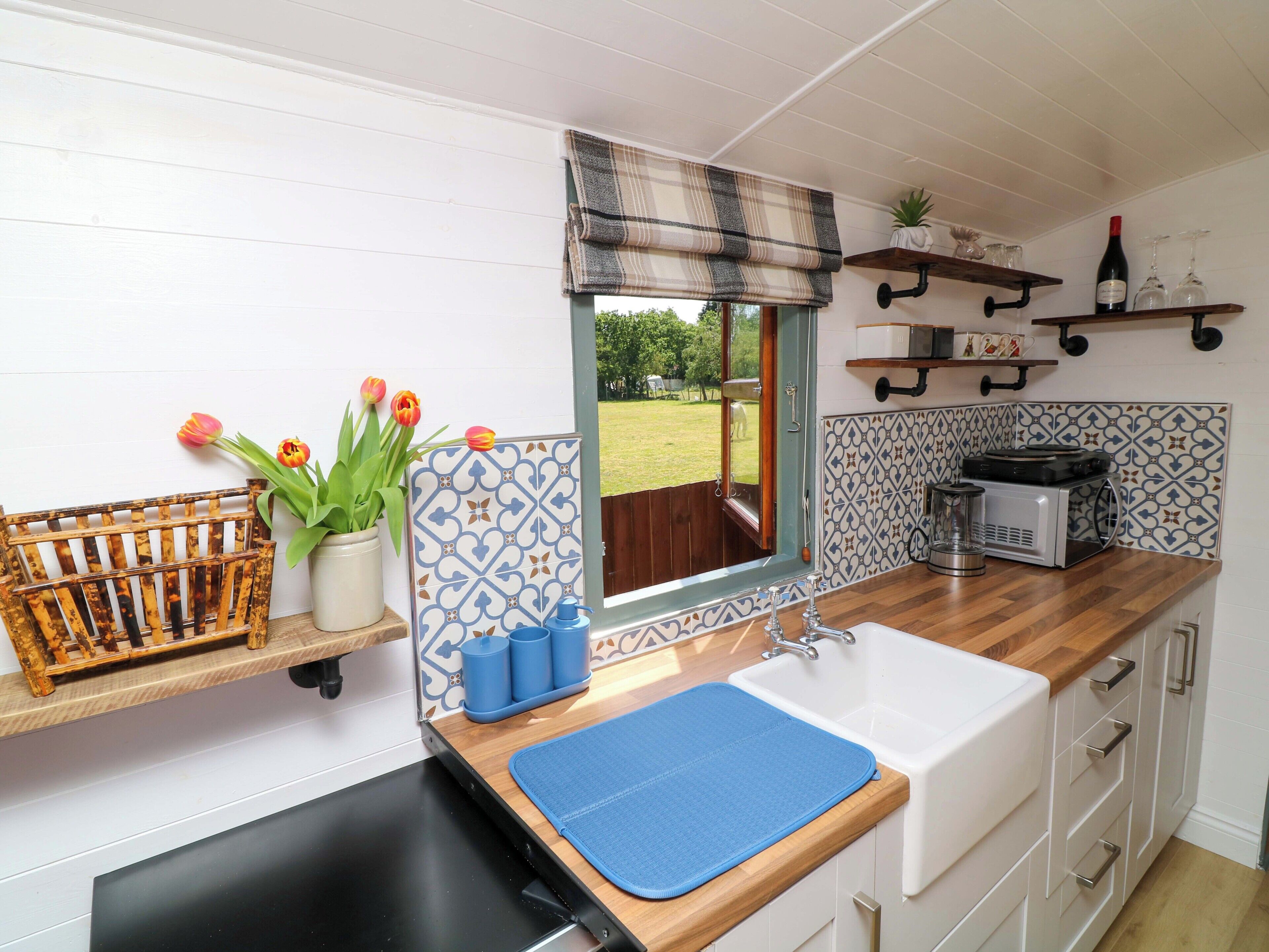 A kitchen with a window, a sink, a microwave, and a shelf with wine glasses.