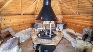 Tunnelmallinen mökin sisustus, jossa on puukamina, turkiksilla päällystetyt istuimet ja puinen katto.