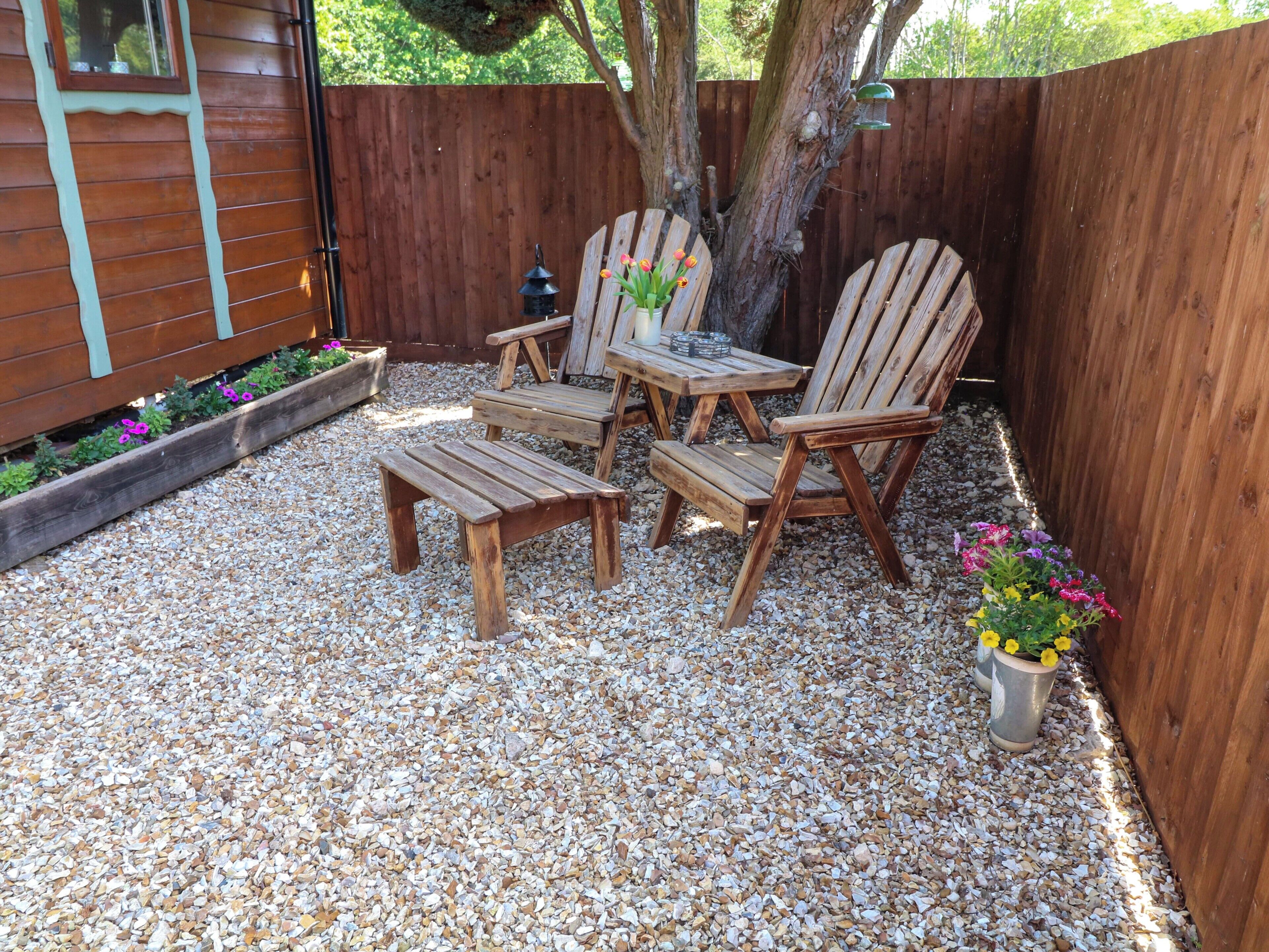 A wooden deck with a table and chairs, surrounded by gravel and potted plants.
