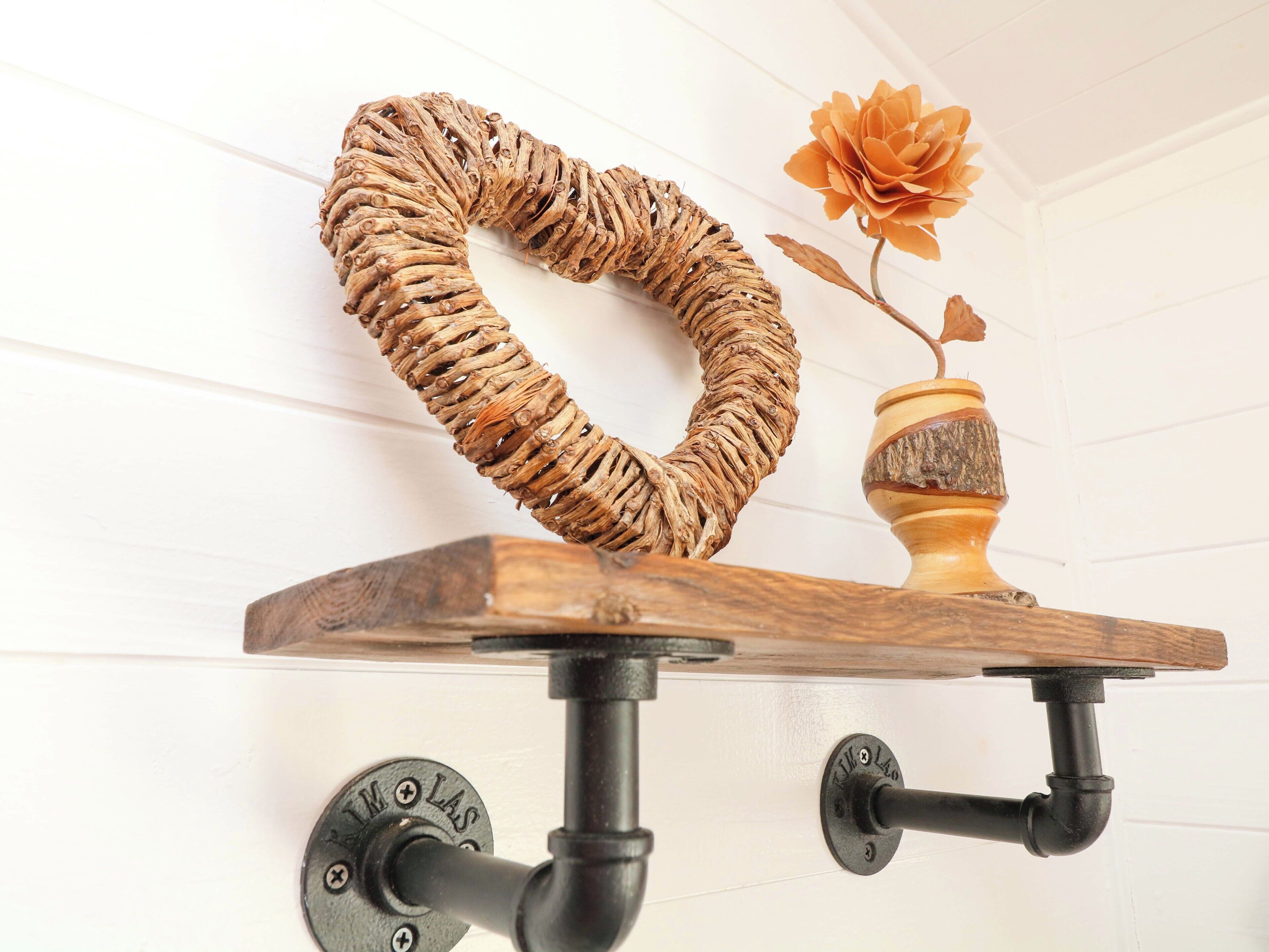 A wooden shelf with a decorative rope item and a vase with a flower.