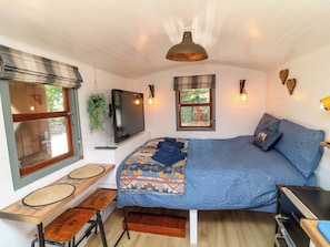 Una habitación acogedora con una cama, un televisor, una mesa con un mantel individual y una banca.