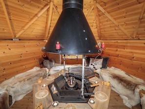 Una estufa de leña con chimenea negra, rodeada de alfombras de piel y muebles de madera.
