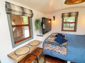 Ein Zimmer mit einem Bett, einem Fernseher, einem Fenster mit Aussicht, einem kleinen Tisch mit Unterlage und einer Bank mit Unterlage.